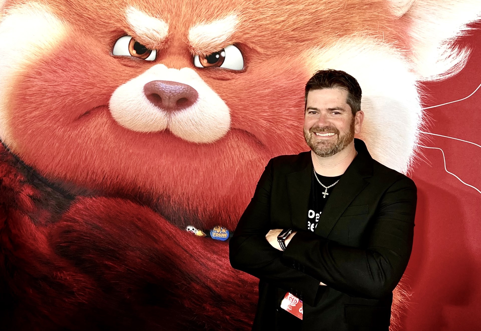 Jacob Brooks smiling in front of a still from Pixar's Red Panda.